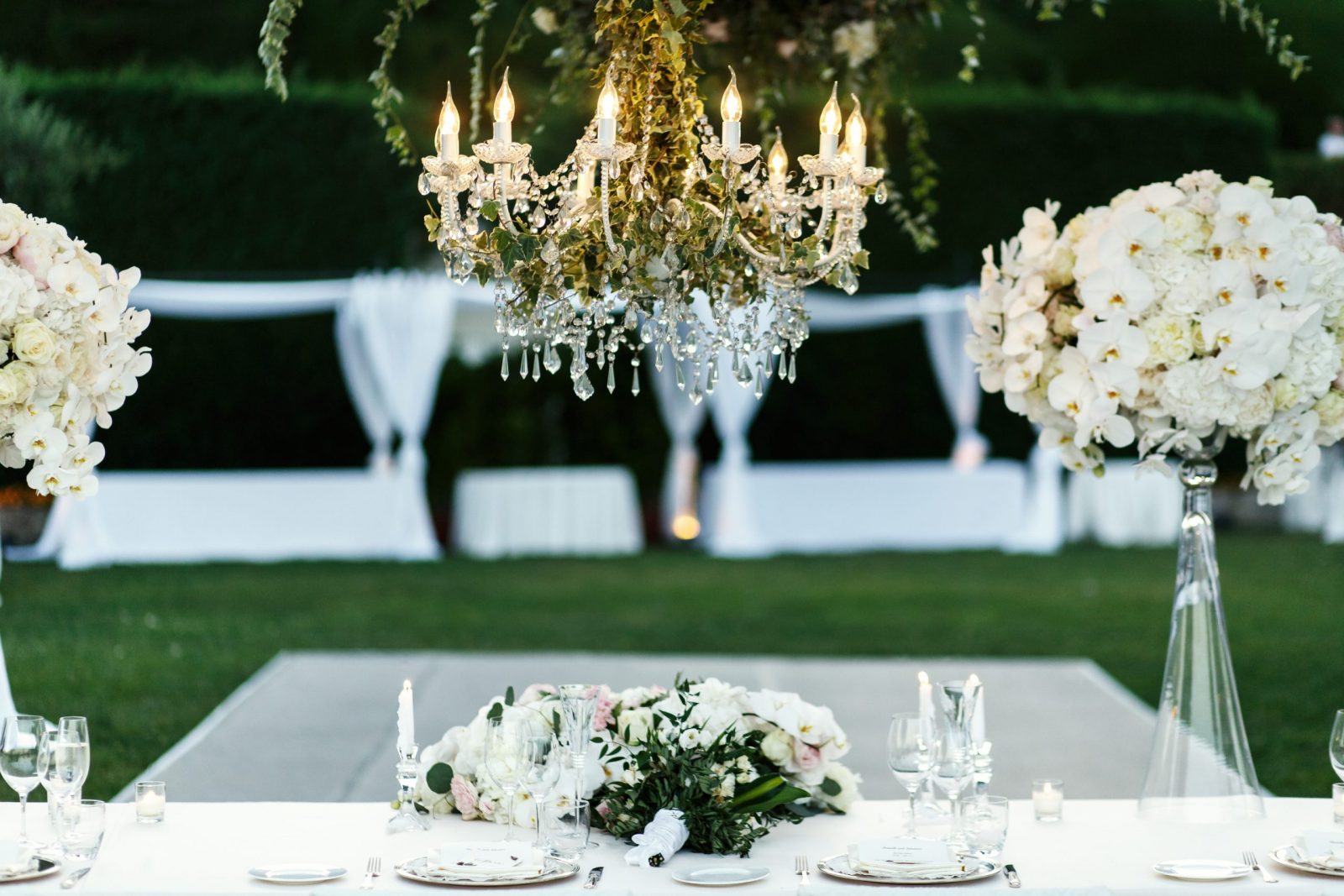 Chandelier with flowers and greenery hangs over dinner table for newlyweds