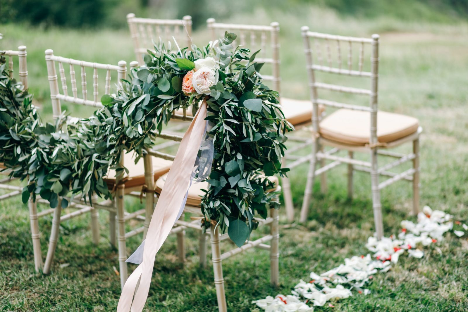 Floral garlands of green eucalyptus and pink flowers decorate wedding arch and chairs on the hill